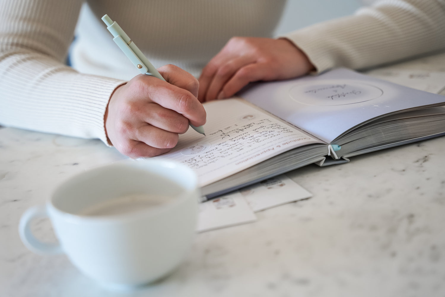 A person writing in their 365 intention journal, using the included sticker pack to customize pages
