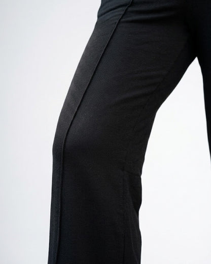 Close-up of black wide-leg trousers worn by a model, showing the side seam and fabric texture against a plain white background.
